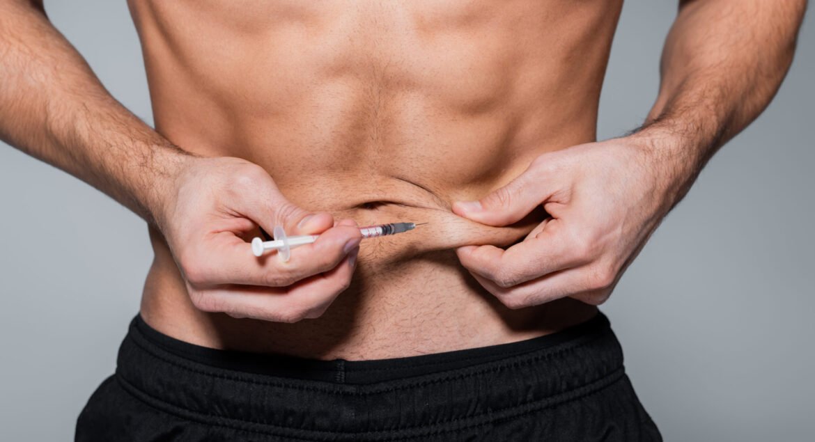 cropped view of shirtless sportsman injecting himself in belly isolated on grey