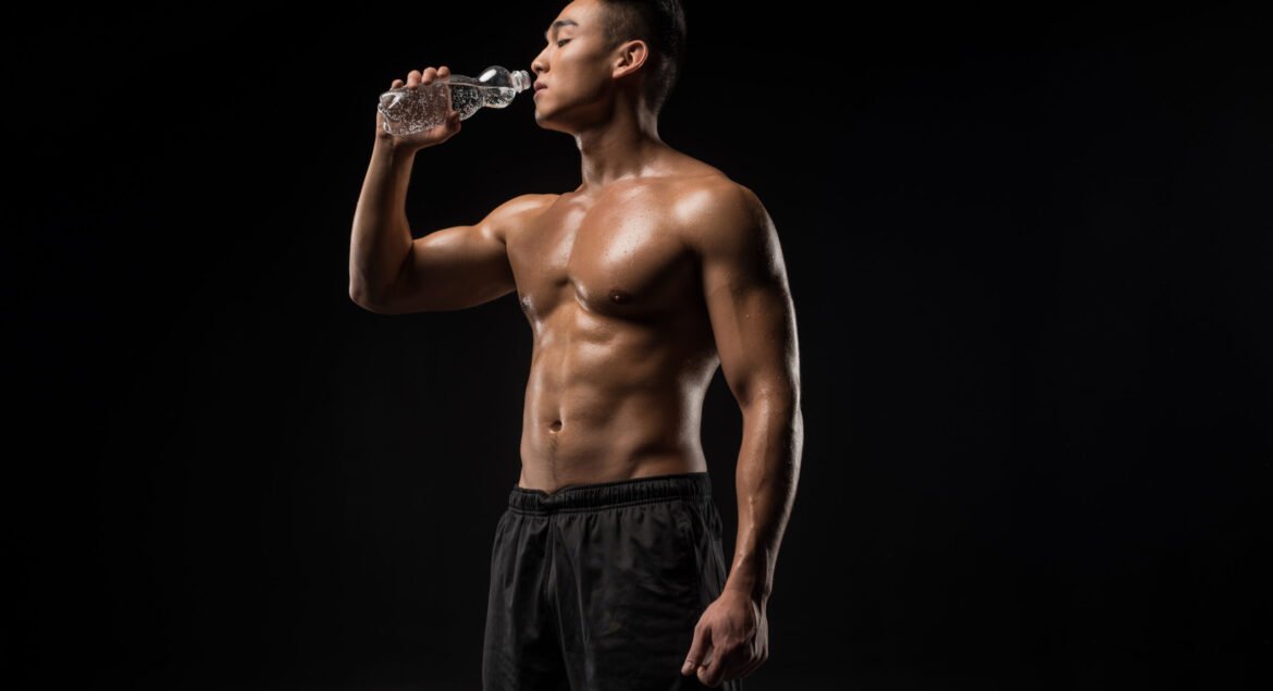 young muscular asian sportsman drinking water isolated on black