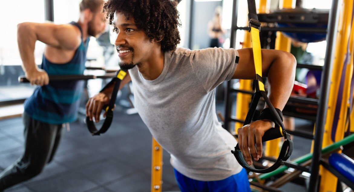 Fit handsome man having fitness TRX training at gym