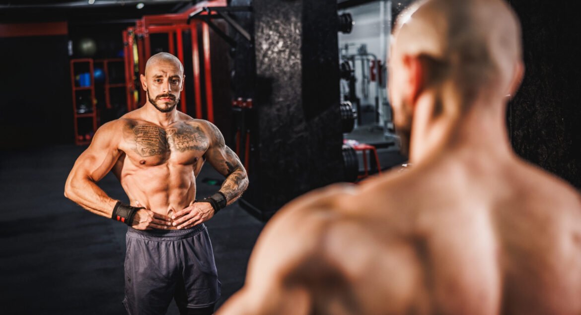 Shot of a young muscular bodybuilder showing his perfect muscles in front of a mirror at the gym.