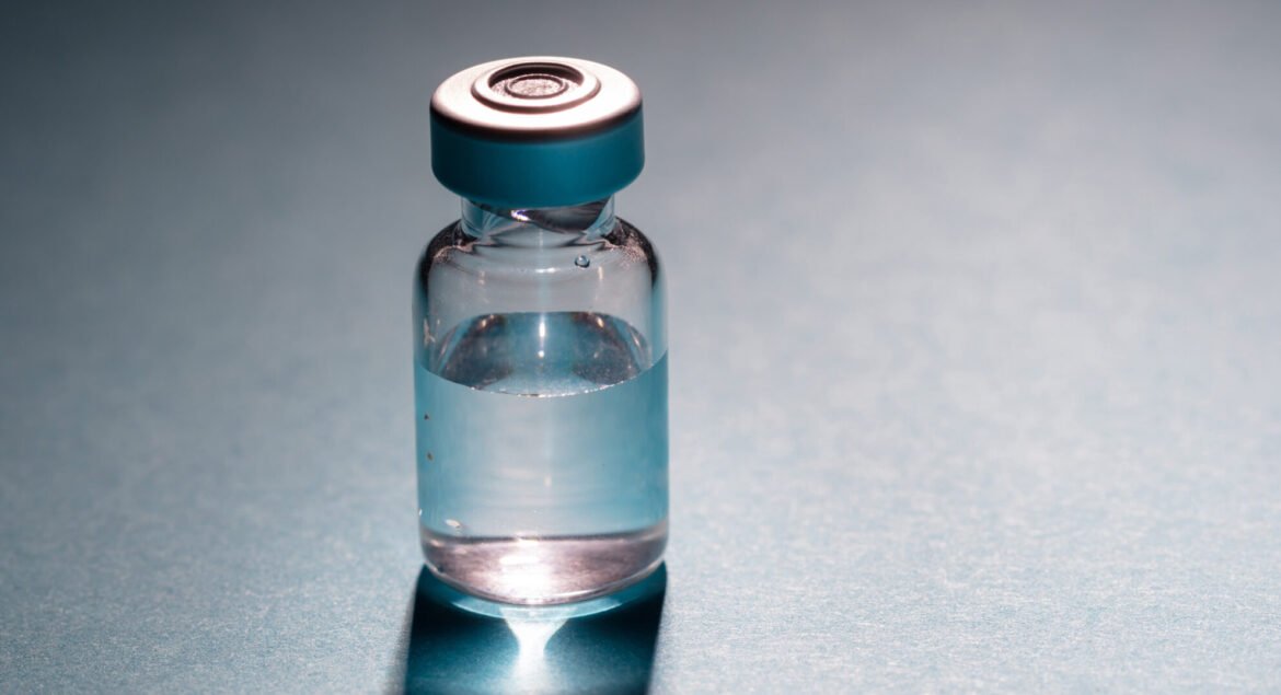 Medical vial for injection on gray blue background, transparent glass bottle, drug medicine vaccine dose. Coronavirus covid-19 flu vaccination concept.