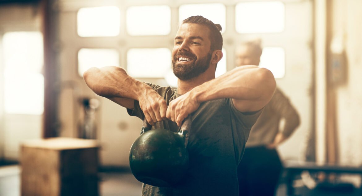 Fit young man in sportswear smiling and working out with a dumbbell during an exercise class in a gym
