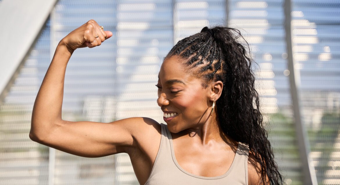 Athletic black woman is flexing her biceps outdoors, embodying strength, fitness, and female empowerment