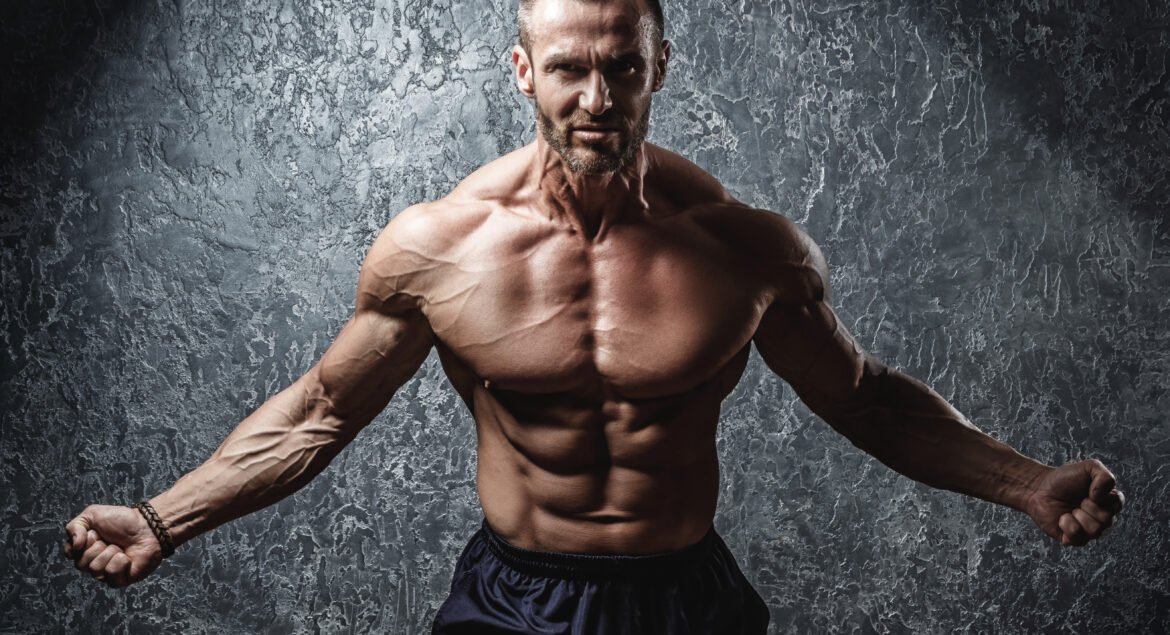 Strong and muscular bodybuilder showing his body near concrete wall