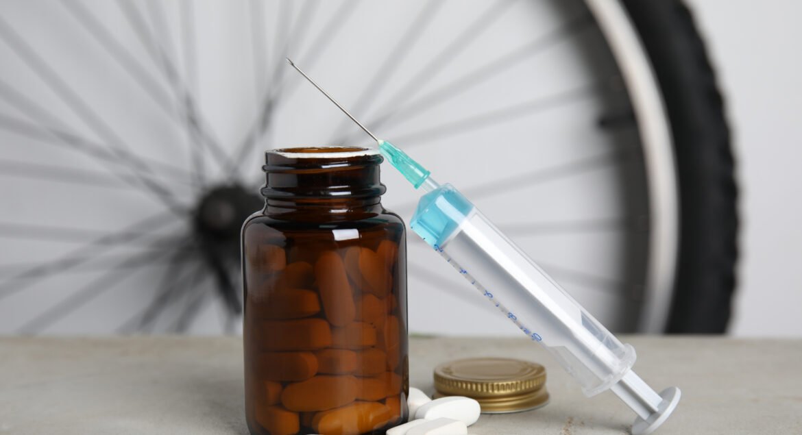 Pills and syringe on light grey table near bike wheel. Using doping in cycling sport concept